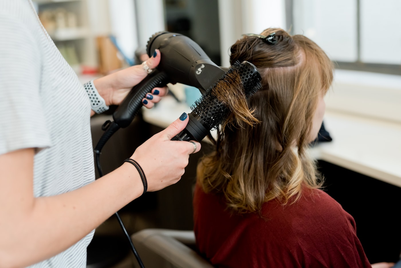 Cabeleireiro usando secador e escova no cabelo da cliente, representando o cabeleireiro formalizado como MEI