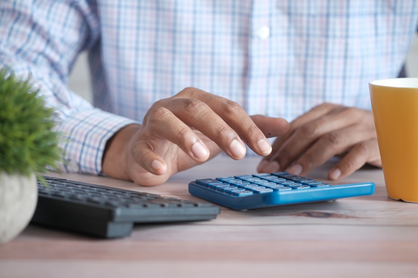 Mãos calculando valores em calculadora na mesa de trabalho, representando o controle de faturamento do MEI
