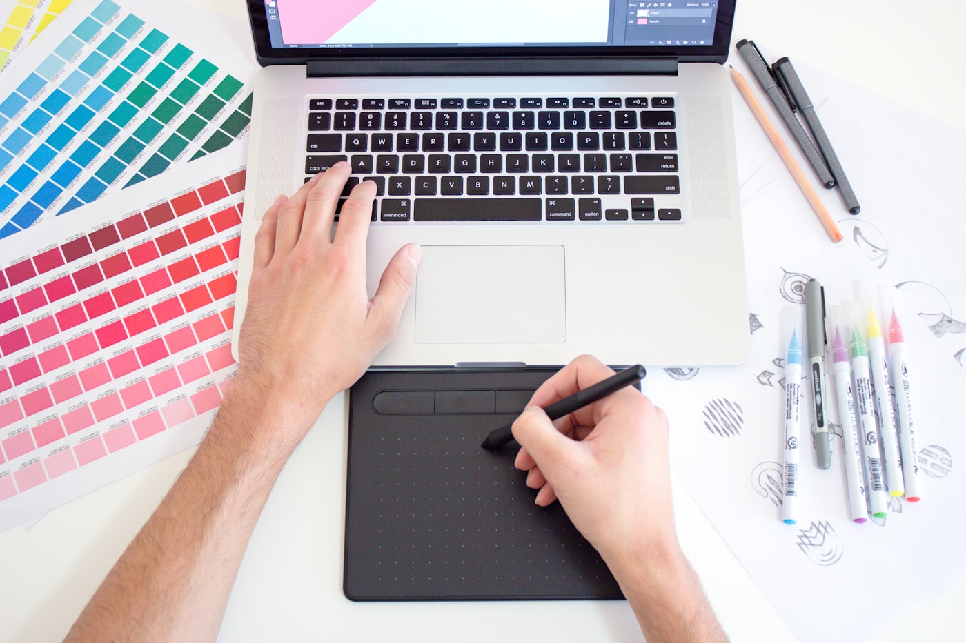 Designer trabalhando em projeto criativo na mesa, notebook e materiais gráficos