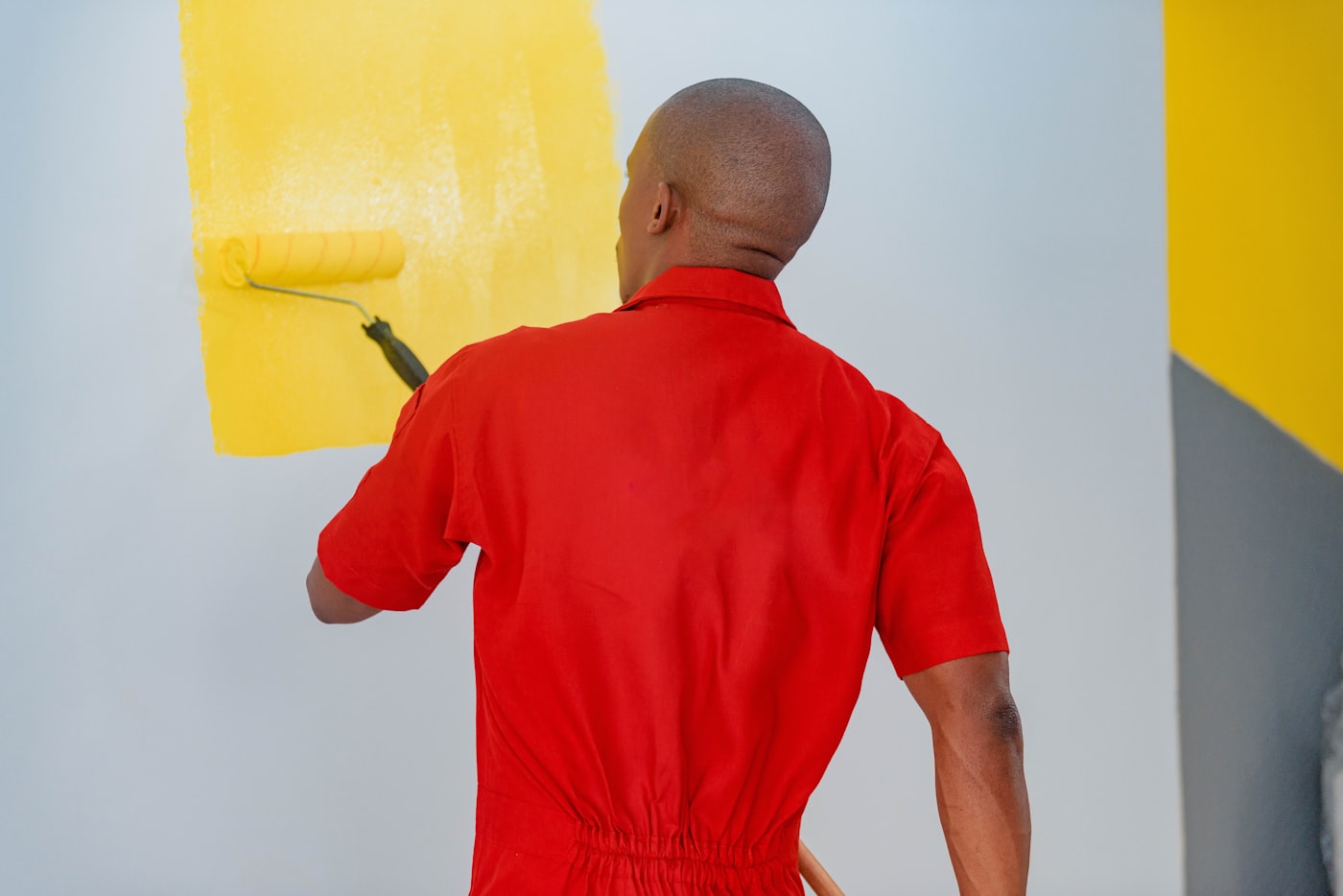 Pintor de macacão aplicando tinta amarela na parede com rolo, representando o pintor formalizado como MEI